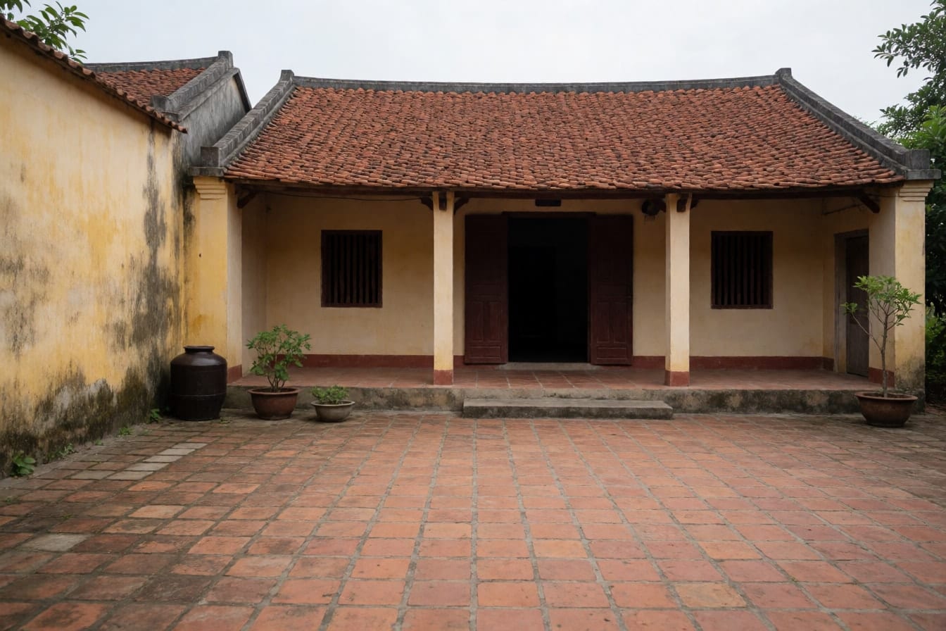 Nhà quê một tầng mái ngói đỏ, hiên cột vuông, tường vàng cũ, sân gạch đỏ trống với chum nước ở góc