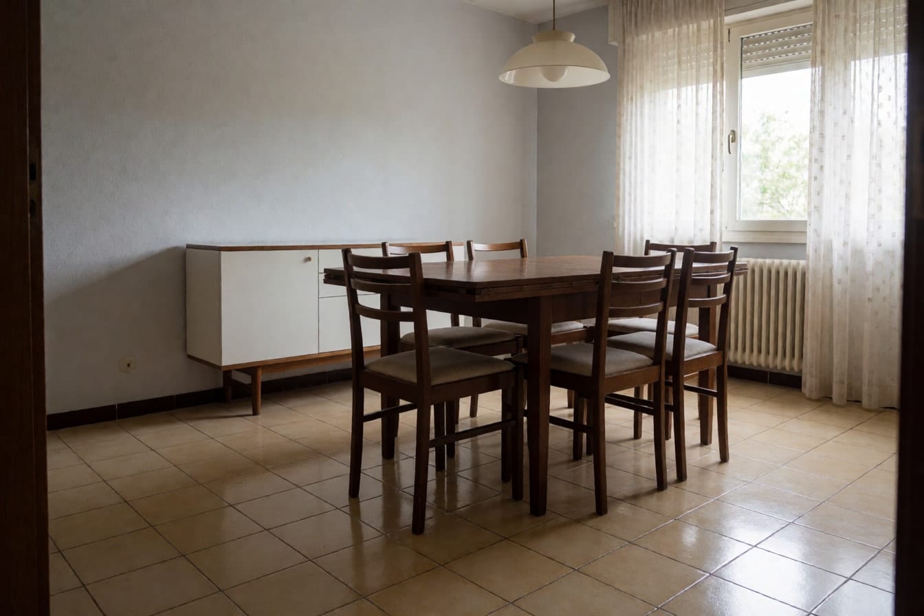 A dining area with shiny beige 1990s floor tiles, a dark wood table with six chairs and a white sideboard