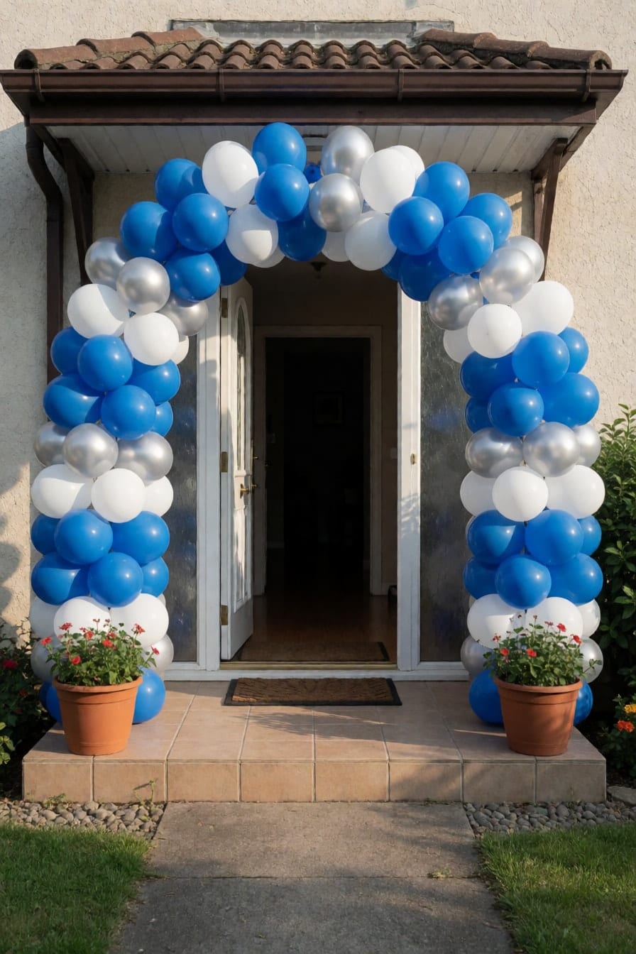 Bilog na balloon arch na asul, puti at silver sa paligid ng bukas na pinto ng bahay, may dalawang paso ng halaman sa beranda