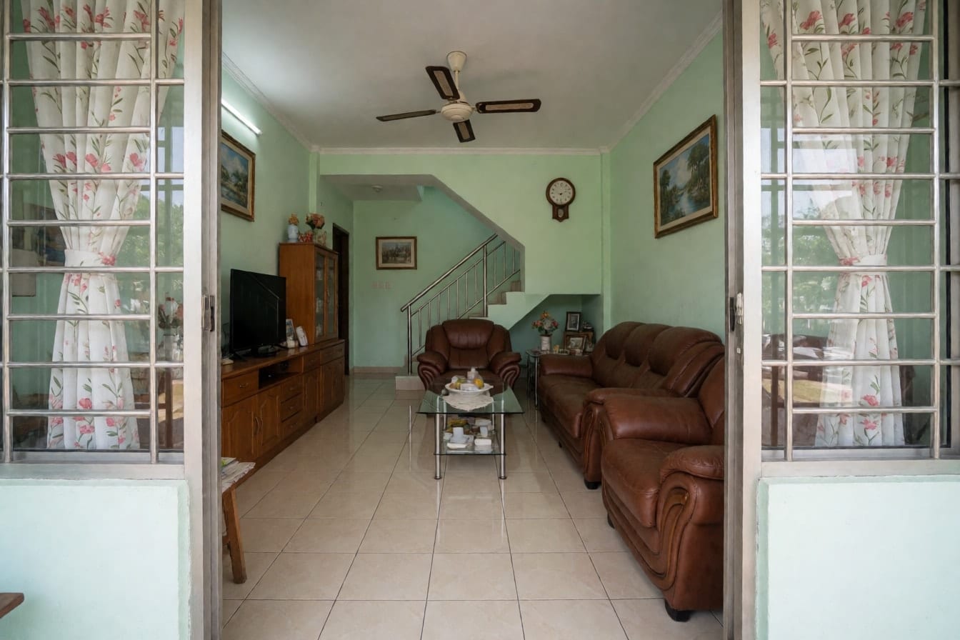 Ruang tamu rumah teres dengan sofa kulit tiruan coklat, meja kopi kaca, kipas siling dan dinding hijau muda