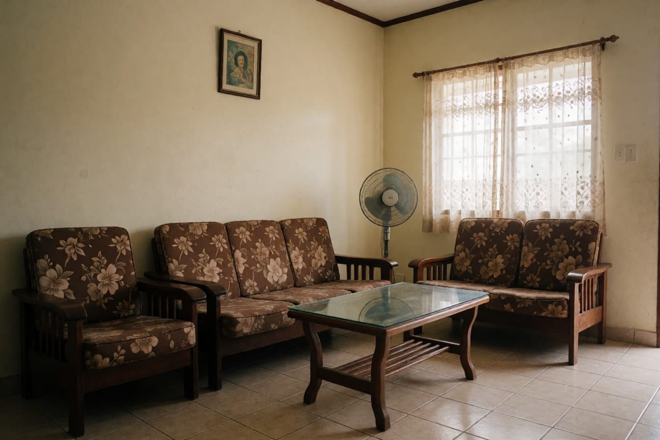 Karaniwang sala ng townhouse na may cream na dingding, kahoy na sofa set na may floral na unan, center table na salamin at electric fan