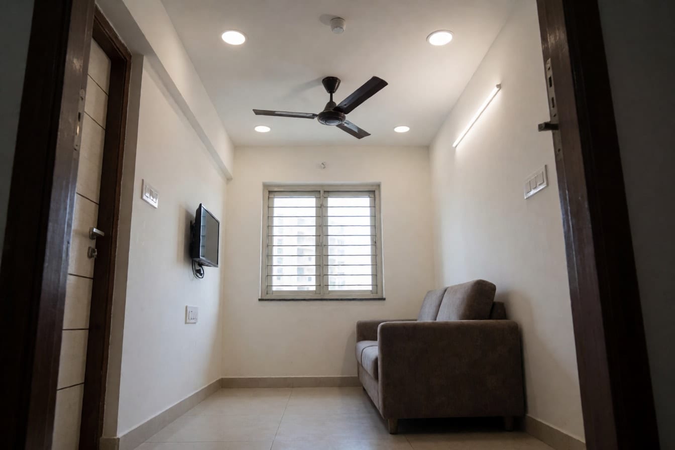 1BHK फ़्लैट का छोटा हॉल: नीची छत पर बहुत पतला POP किनारा, एक पतली गर्म लाइट लाइन, स्लिम डाउनलाइट और छत से सटा पंखा