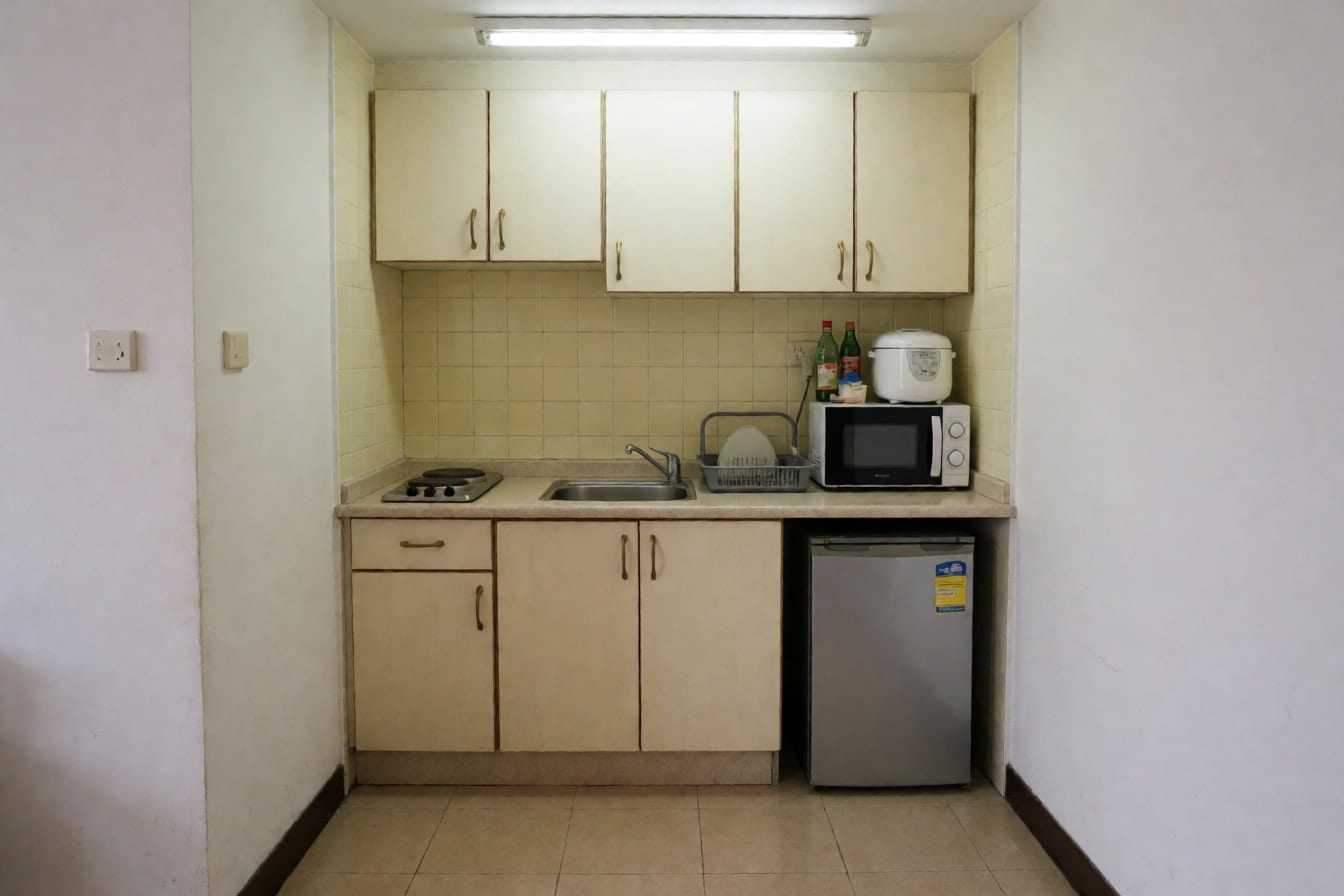 Lumang kitchenette ng studio na may cream na cabinet, maliit na lababo, de-kuryenteng kalan, microwave at maliit na ref