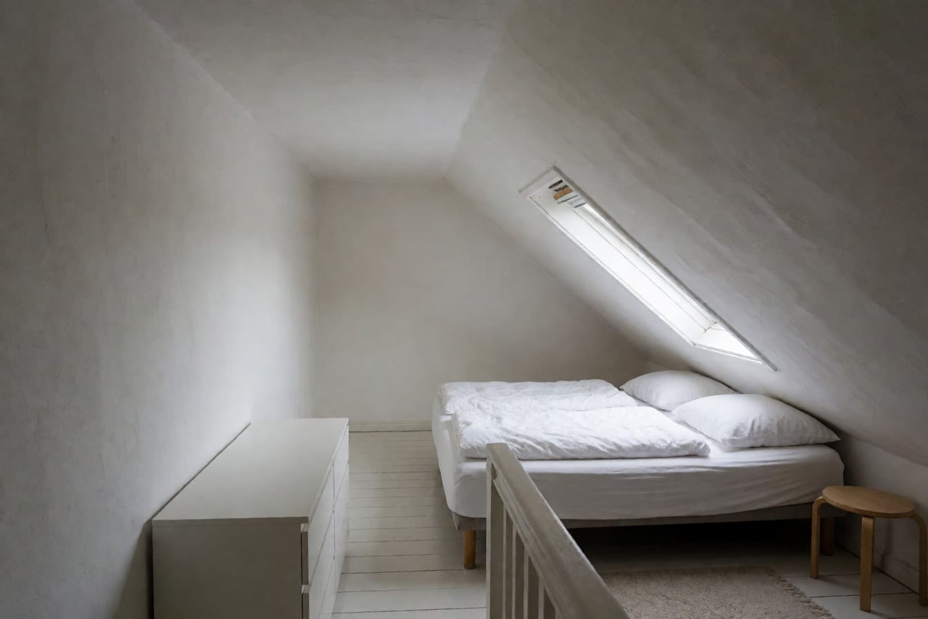 Ett vindssovrum med vitt snedtak, takfönster, låg säng under snedden och vitmålat trägolv