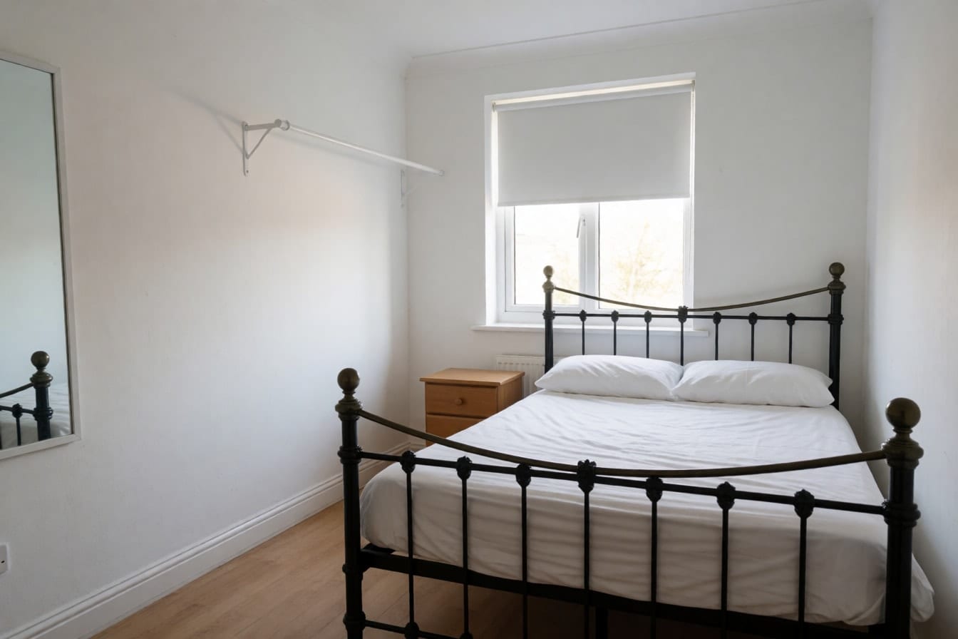 A rental bedroom with bright white walls, a black metal bed and a clothes rail