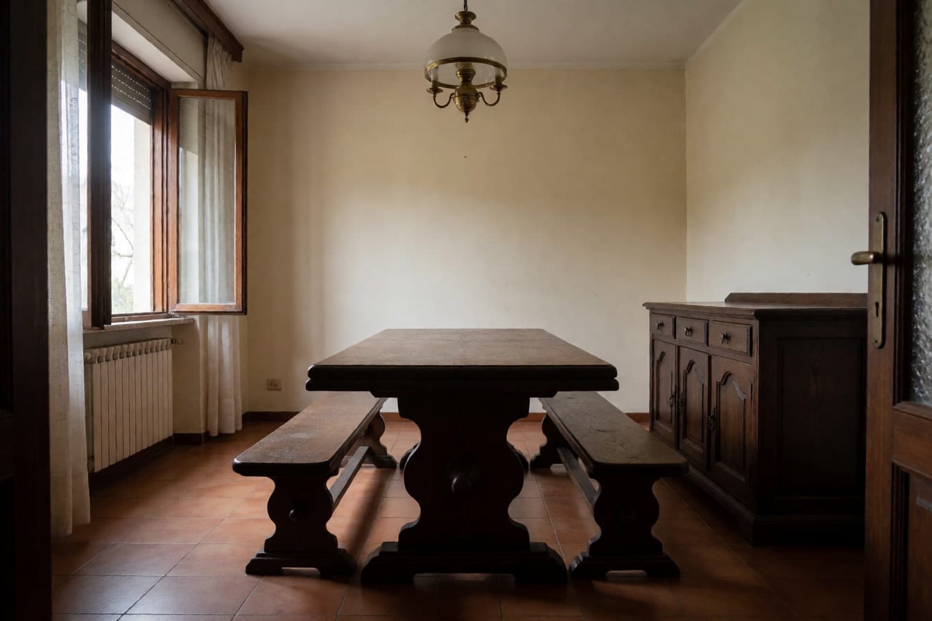 Esszimmer in einem älteren Haus mit dunklem Holztisch, zwei Bänken, Anrichte, Messinglampe und Terrakottafliesen